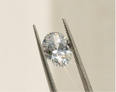 Tweezers holding sparkling oval diamond