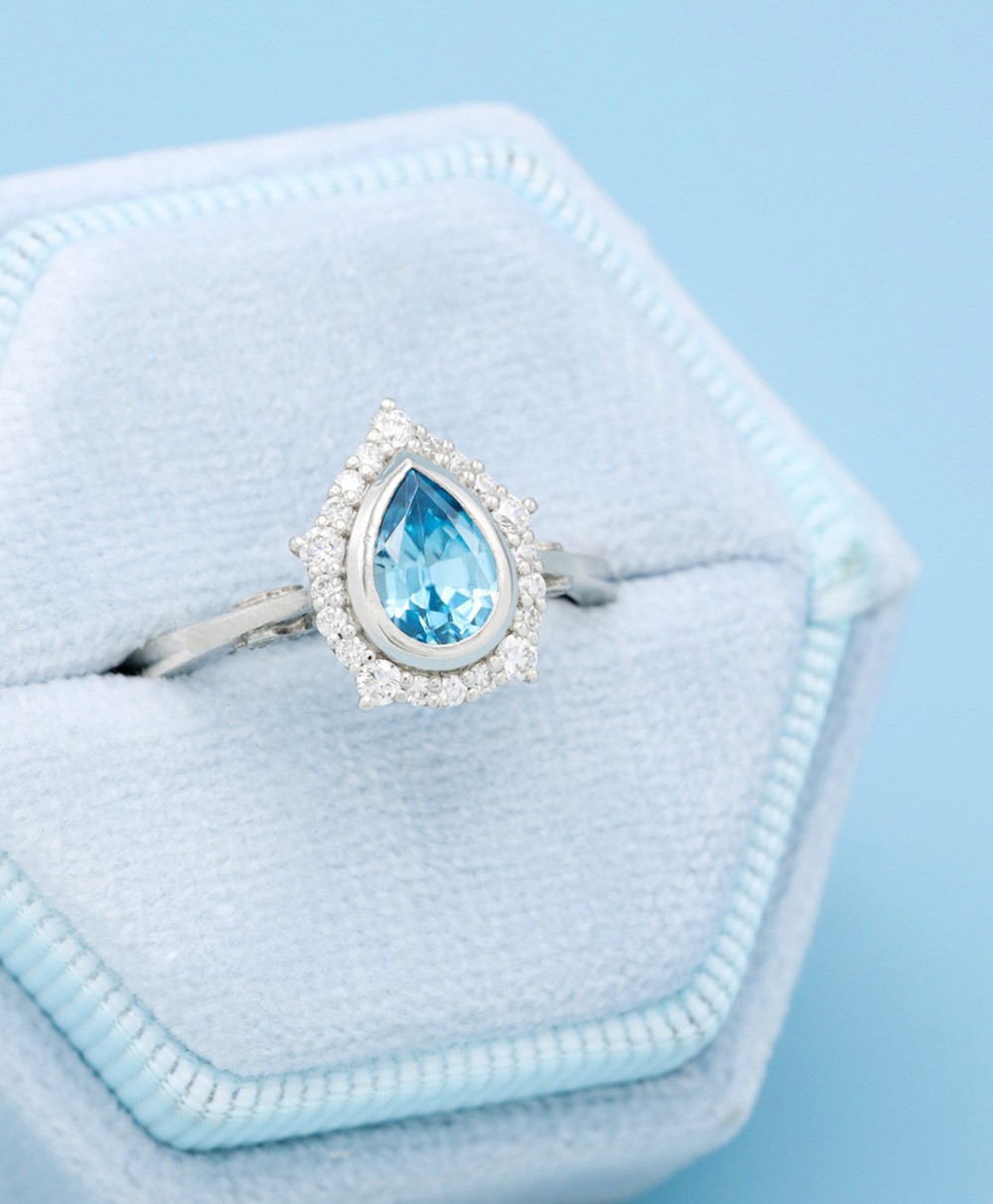 Pear-shaped blue gemstone engagement ring in light blue velvet box.