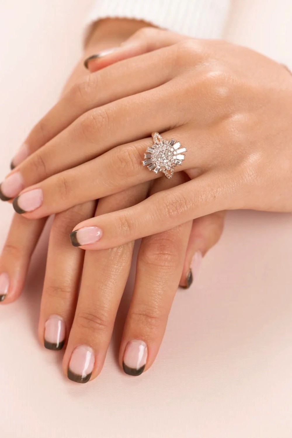 Close-up of hands with overlapping fingers showing diamond cluster engagement ring.